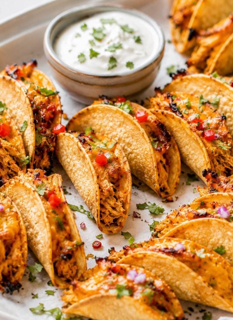 A close-up view of baked chicken tacos with crispy shells, filled with shredded chicken and topped with diced tomatoes and chopped cilantro.